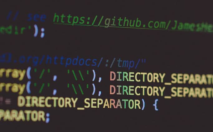 A close-up of hands typing on a keyboard in front of lines of code on a monitor