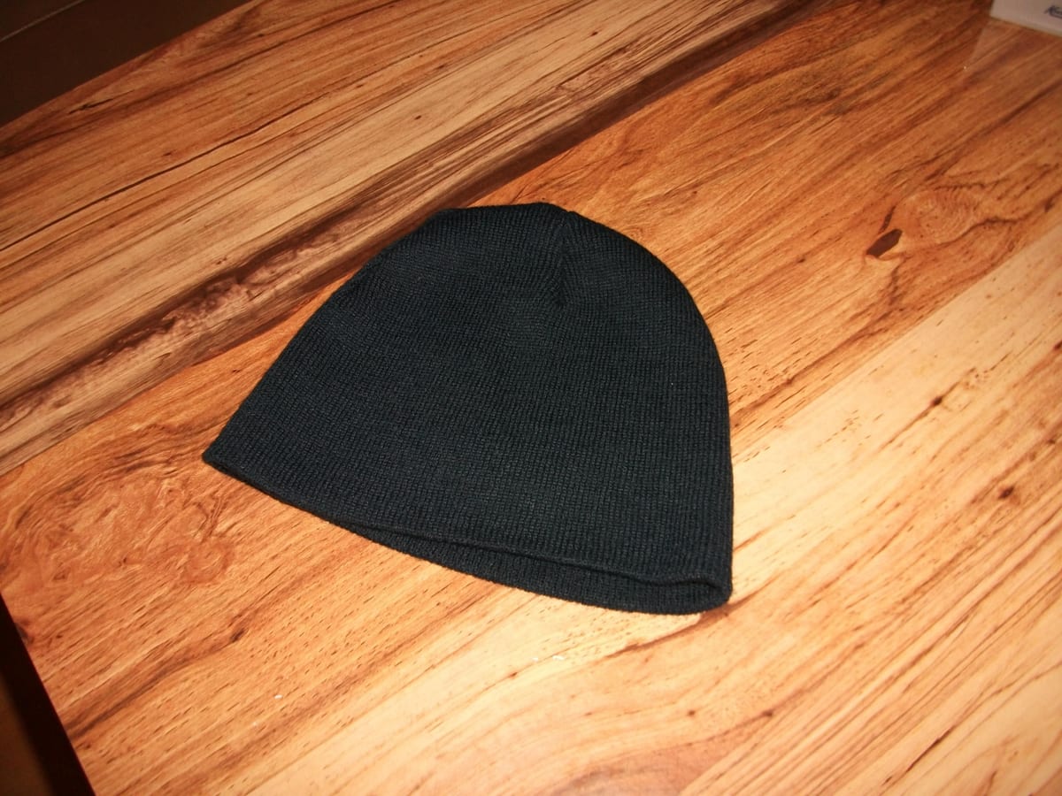 The original phone photo: a plain dark navy-black knit beanie with no cuff lying on an orange-brown wooden table, lit by camera flash
