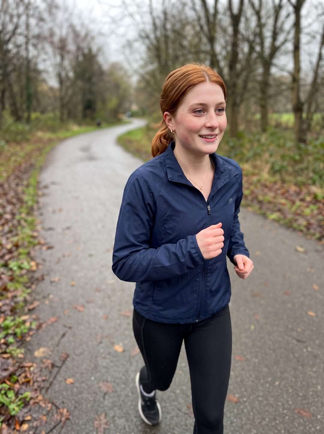 AI photo of the woman jogging on a leafy park path in a navy running jacket with her hair in a low ponytail
