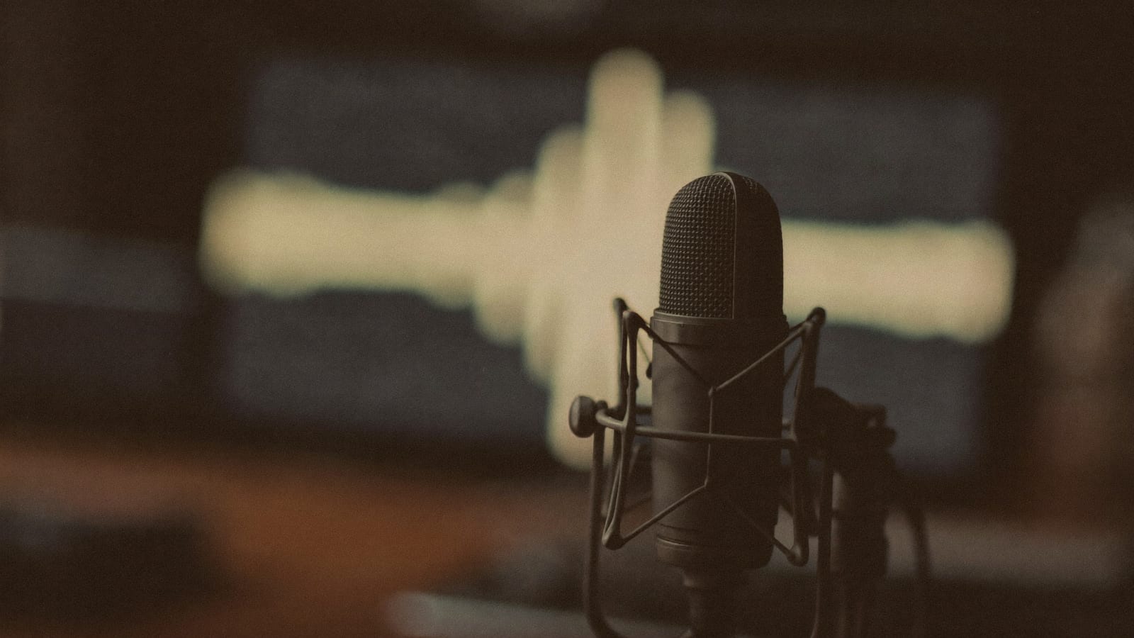 A moody close-up of a studio microphone on a desk with soft glowing audio-waveform light behind it