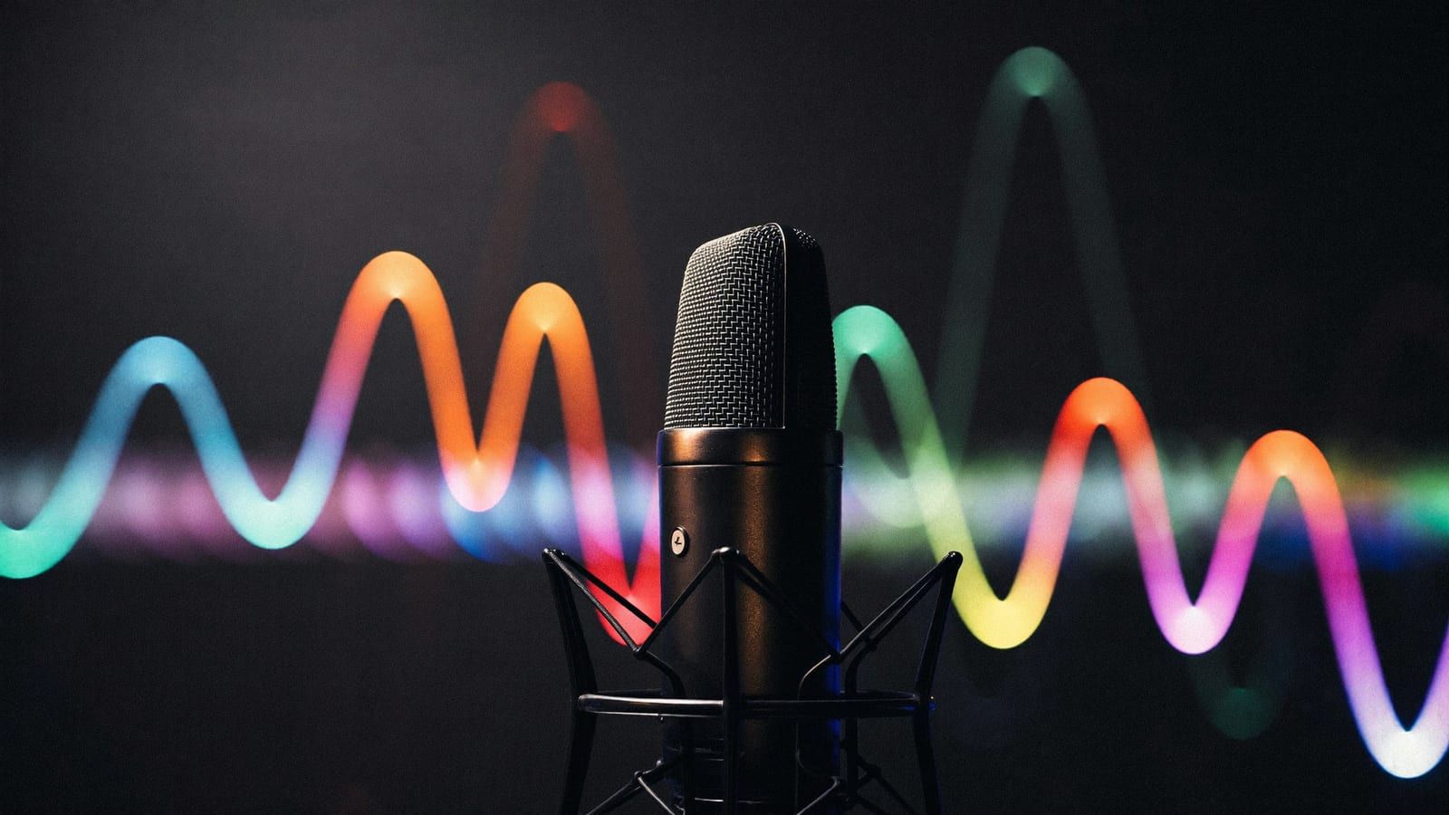 A dark desk lit by a glowing audio waveform on a laptop screen with headphones beside it