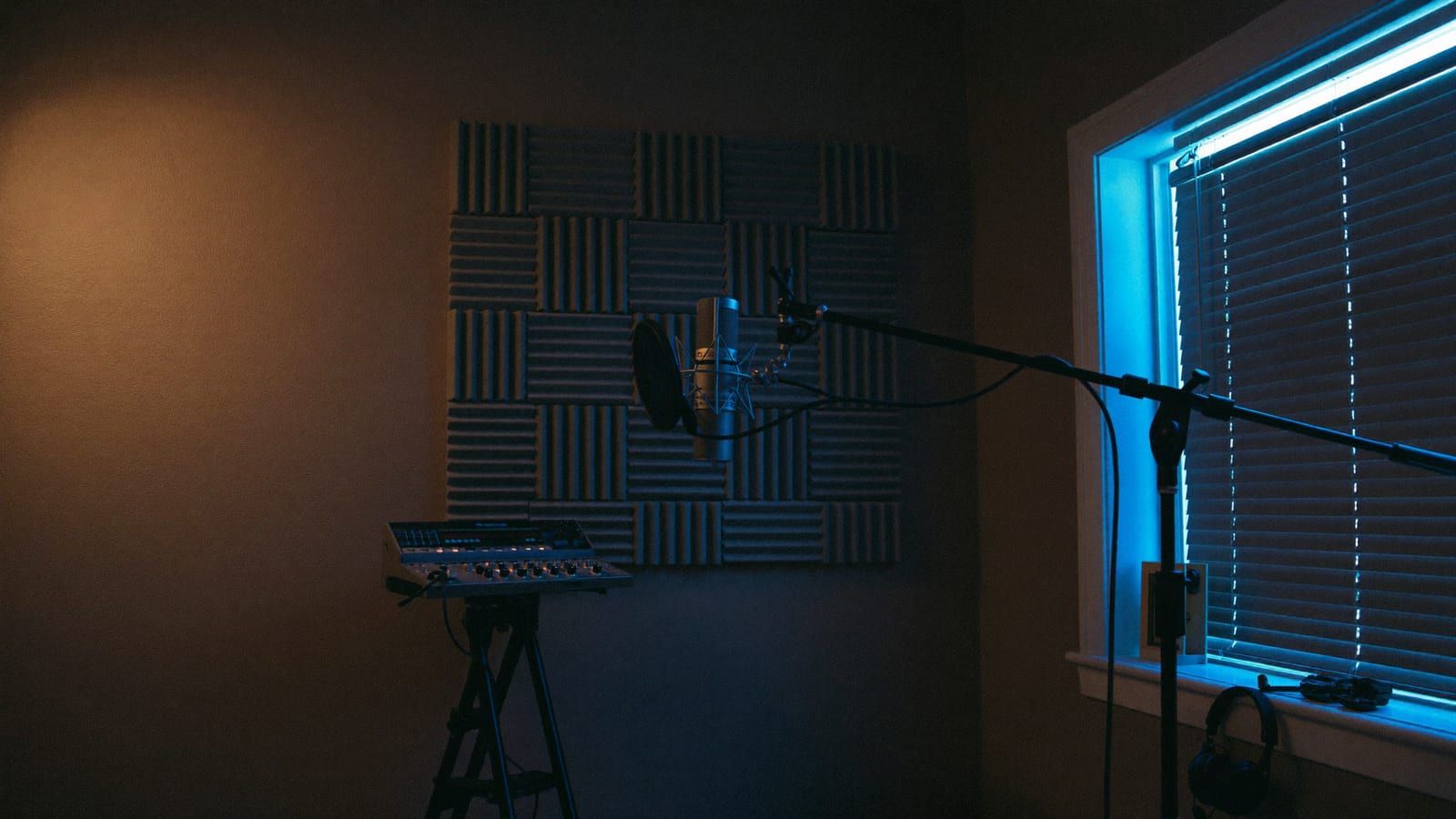 A cozy home recording corner with a microphone on a boom arm, soft acoustic panels and a warm lamp