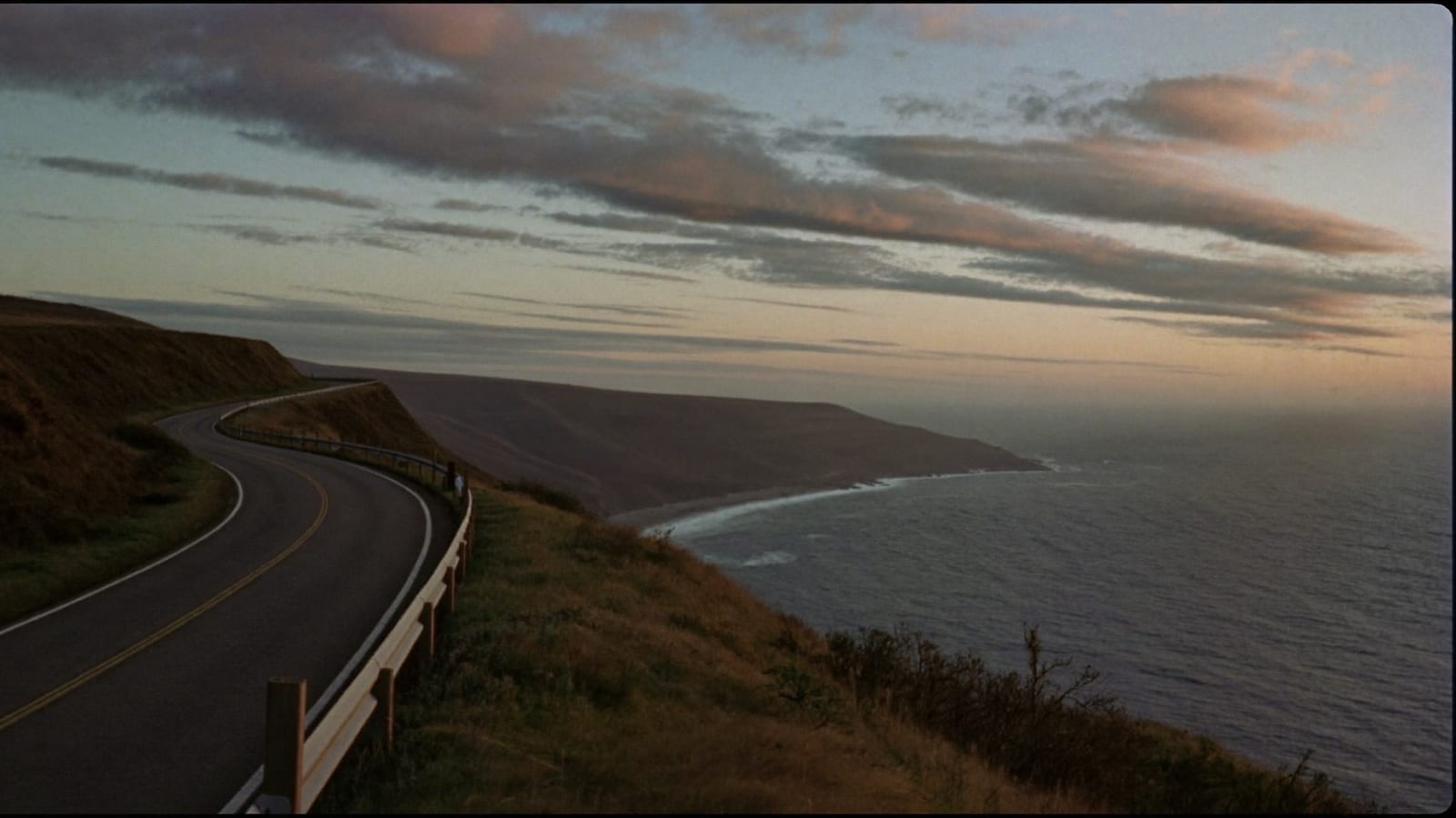 A cinematic aerial still of a coastal cliff road at dawn, a still from a Higgsfield generation