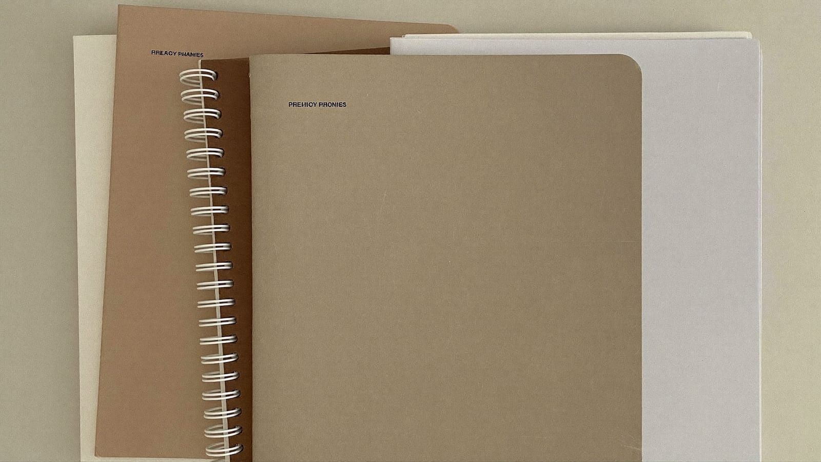A stack of plain, minimalist blank-cover journals and planners in warm neutral tones