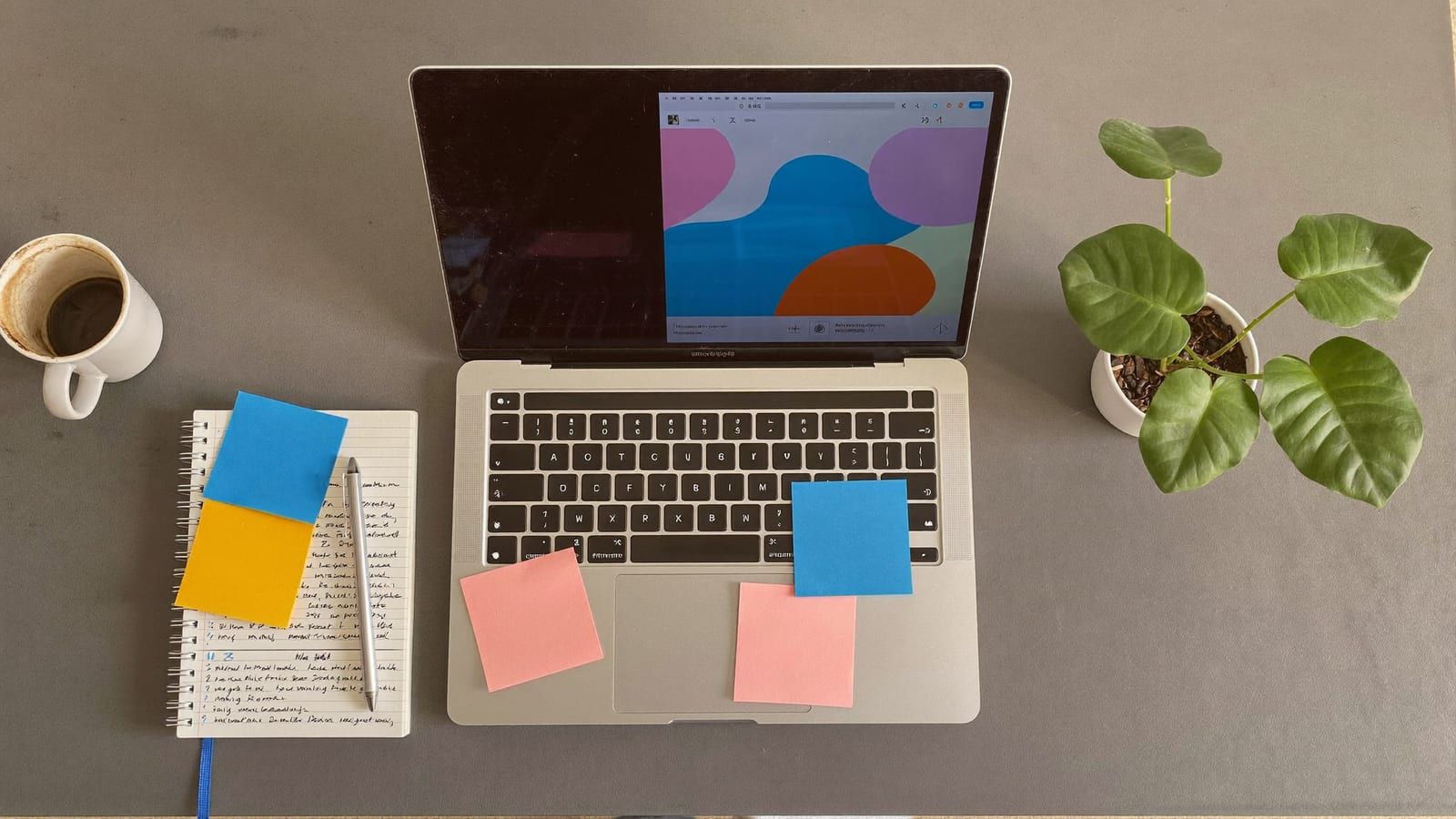 A tidy prompt creator's desk from above with a laptop, coffee and a notebook