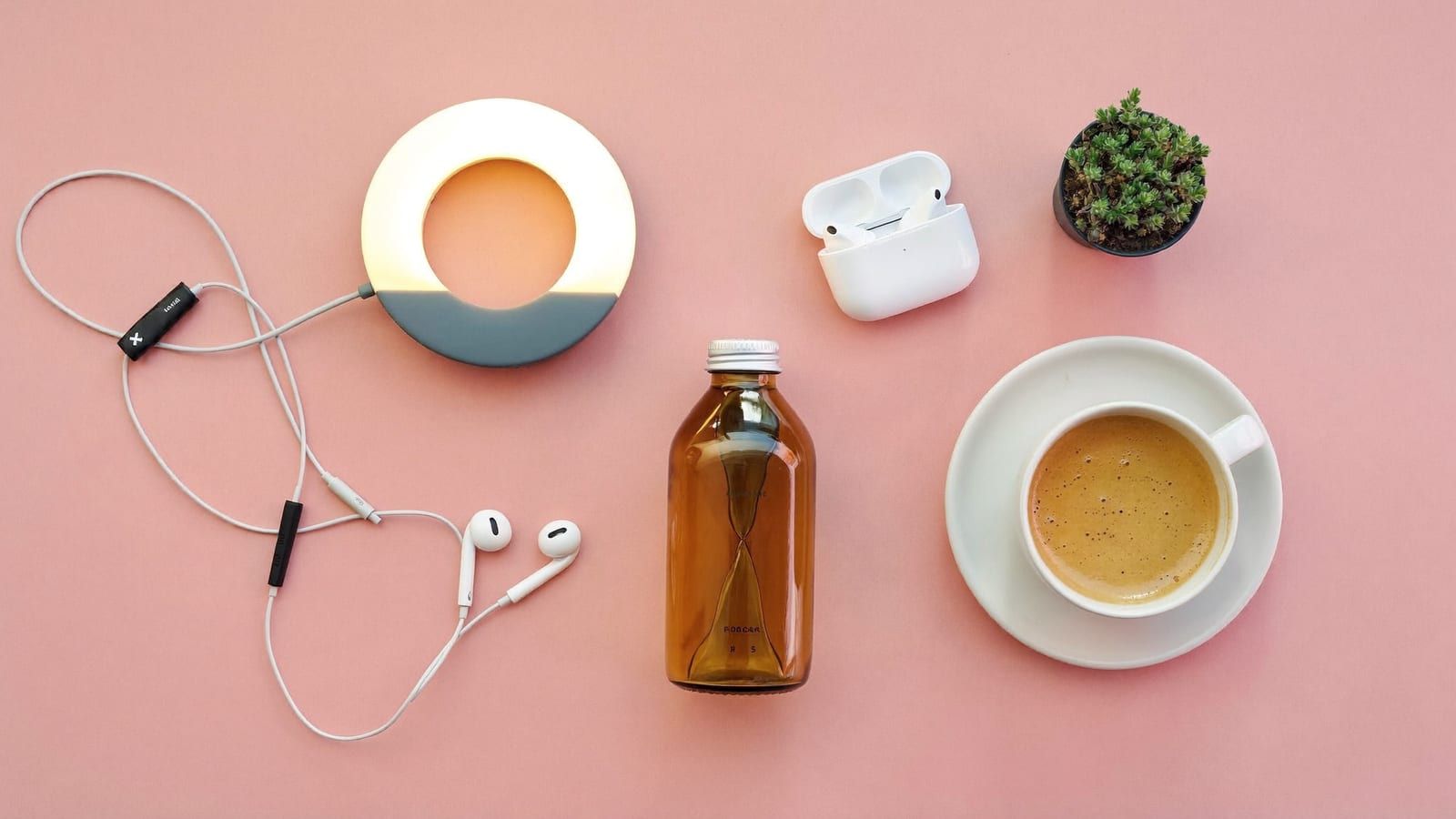 A creator's desk flat lay: a ring light, wireless earbuds, a plain product bottle, a coffee and a small plant