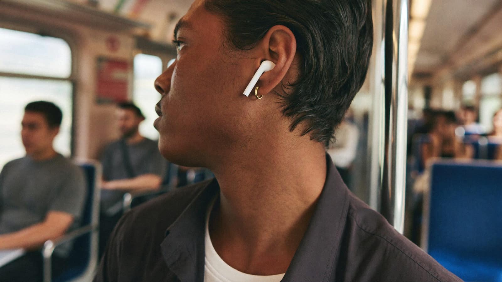 A commuter on a train wearing small white wireless earbuds