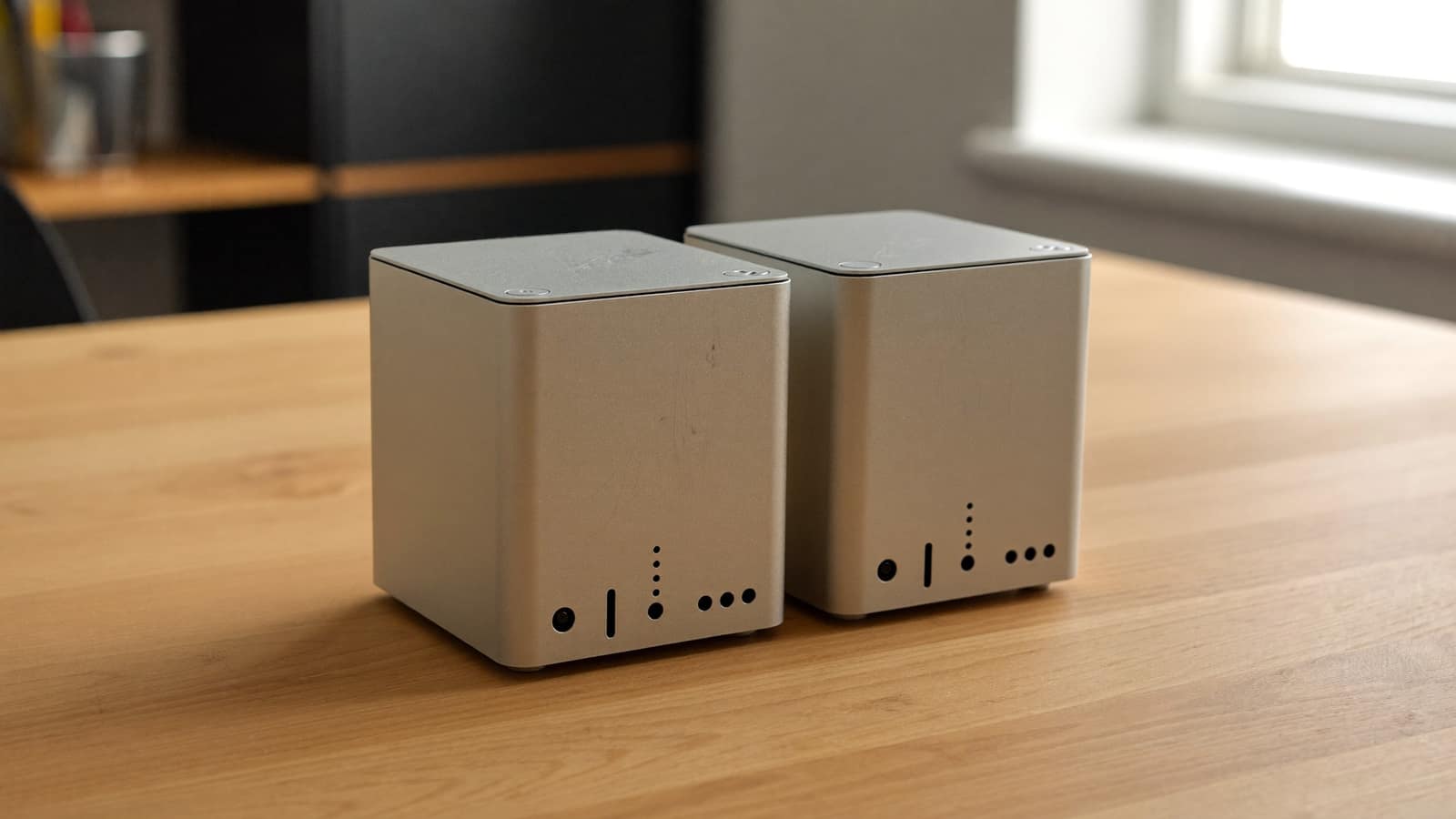Two small silver mini desktop computers side by side on a wooden desk