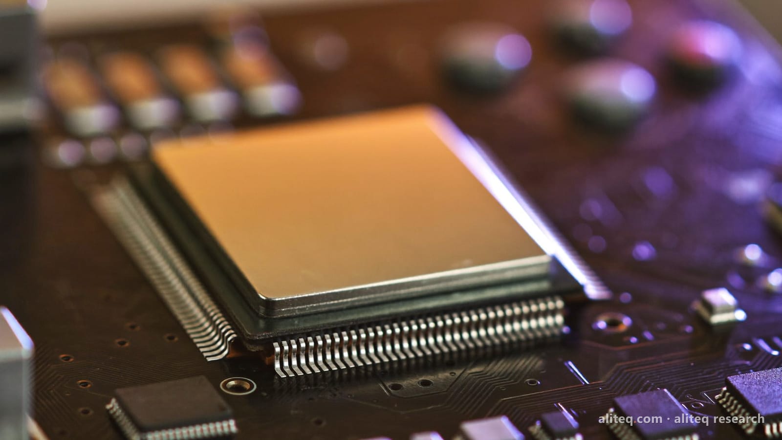 Close-up photo of a bare square processor chip with a metal lid on a dark circuit board, lit warm amber on one side and violet on the other